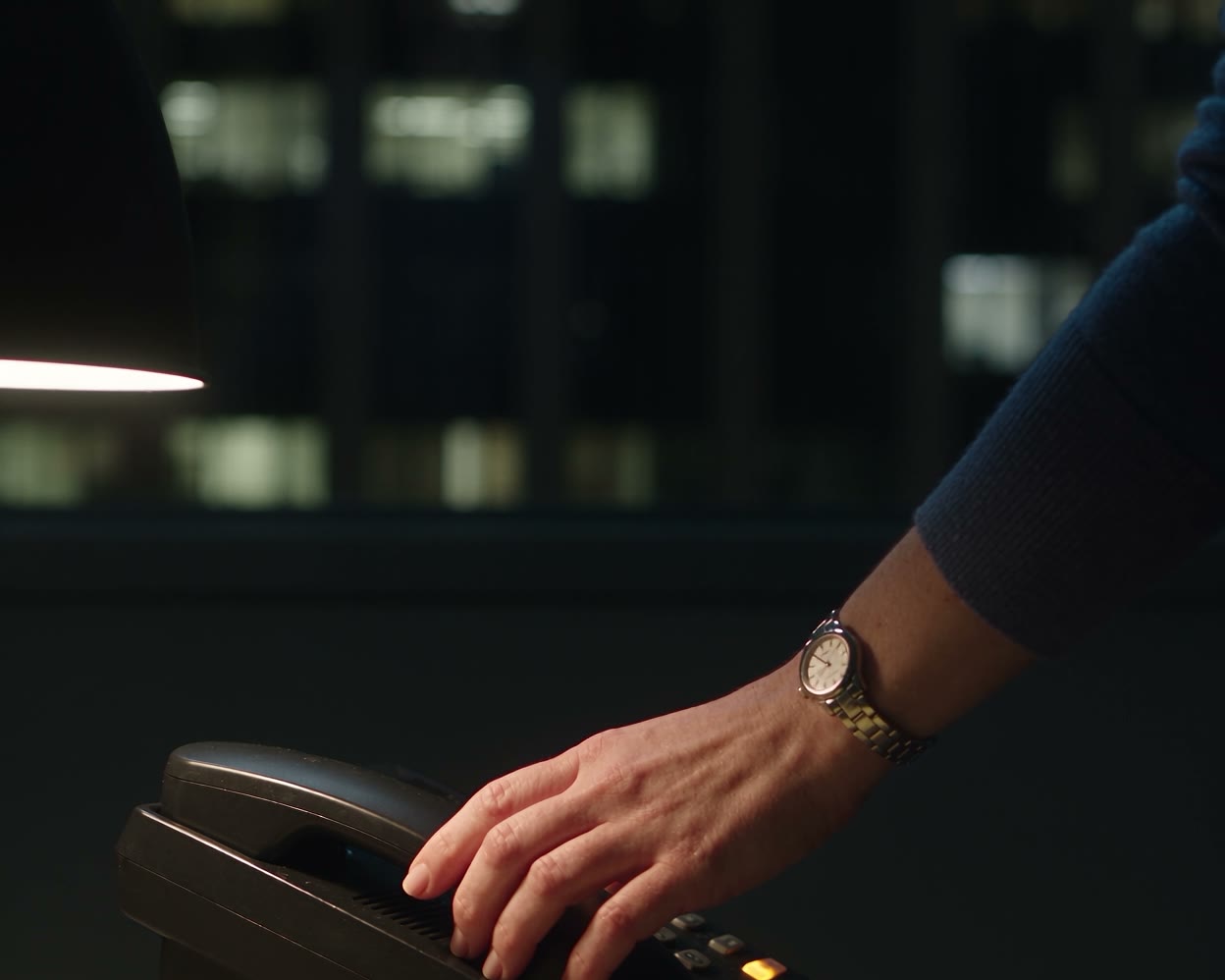 A hand on a desk telephone at night