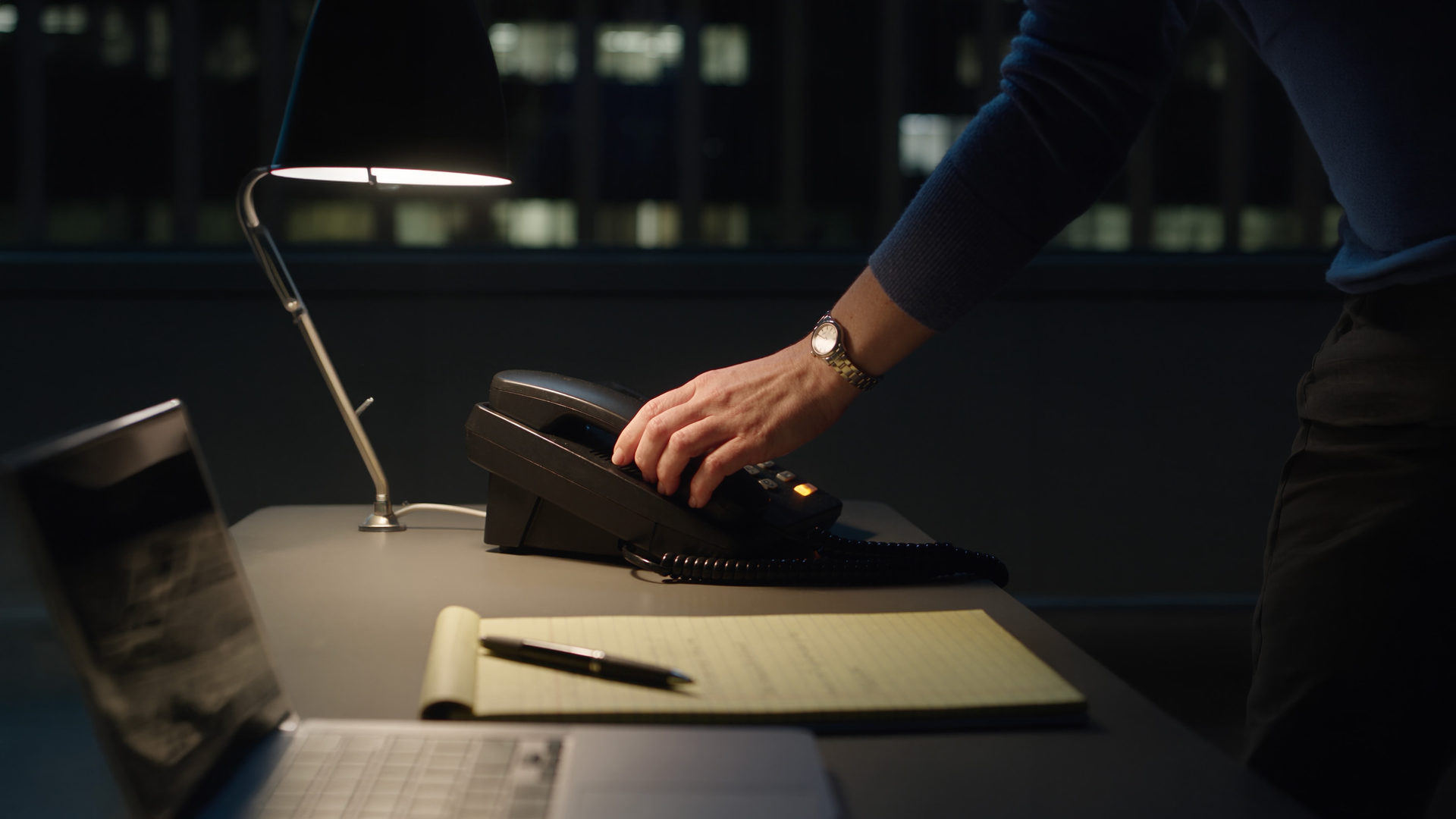 A hand reaching for a desk telephone at night