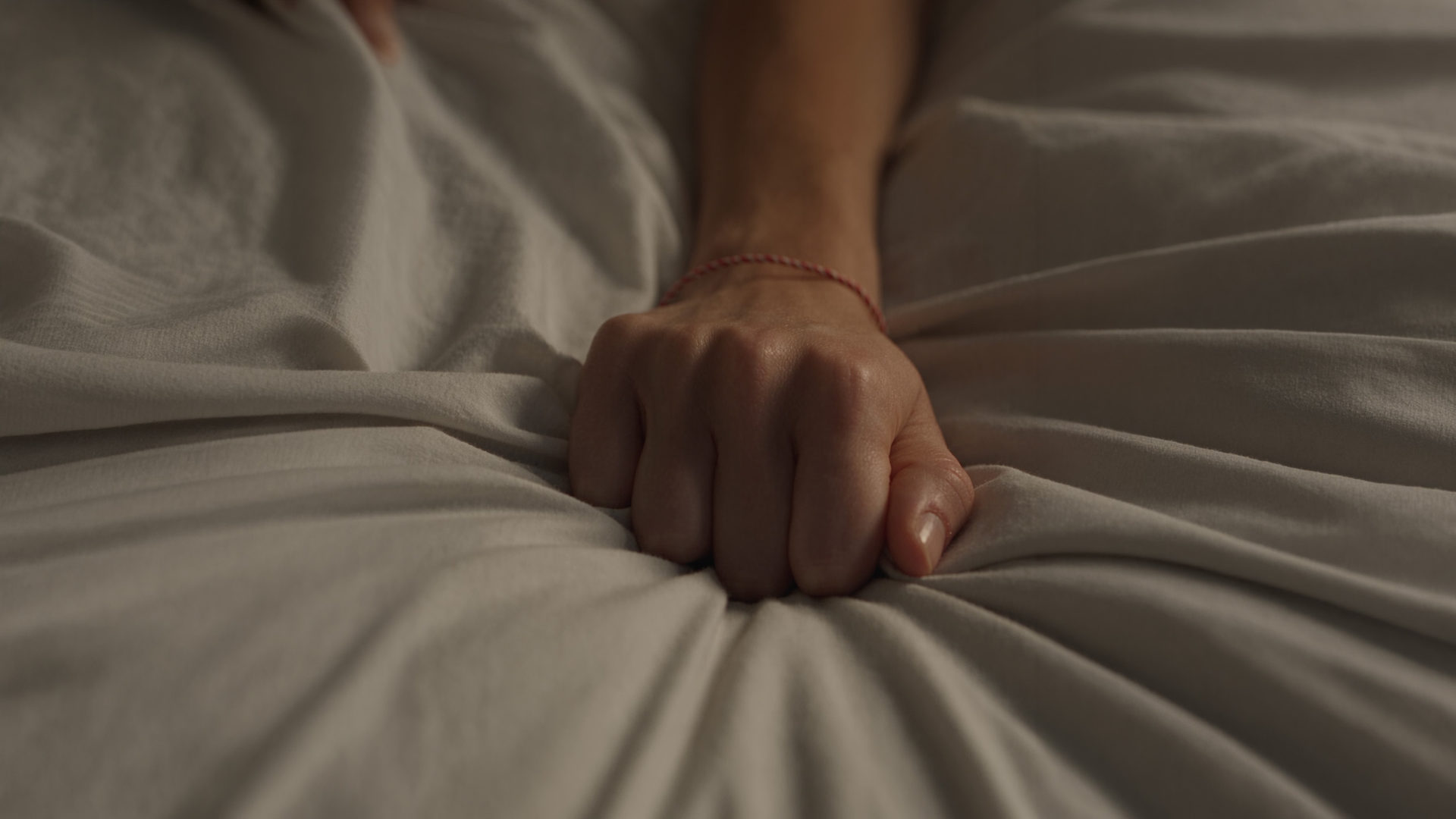 A hand gripping a hospital bedsheet